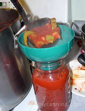 Spooning spaghetti sauce into a canning jar.