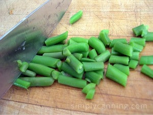 Chopping green beans into smaller pieces using a large chef knife.