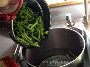 Pouring hot green beans into a bowl of ice water that is sitting in the sink.