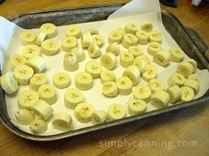 Slices of bananas layered over a freezer paper lined cookie sheet.