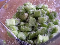 Coating green rhubarb pieces with sugar in a bowl.
