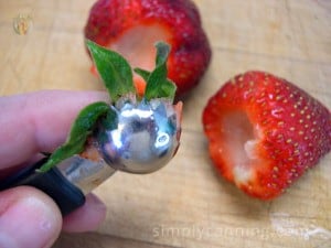 Strawberry huller holding a stem with stemmed strawberries sitting in the background.
