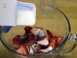 Sprinkling white sugar over a dish of strawberry slices.