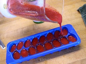 Pouring pink strawberry puree into blue ice cube trays.