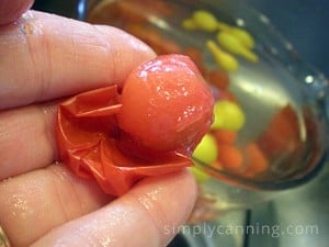 Peeling skins from frozen cherry tomato with the bowl of frozen cherry and pear tomatoes sitting in the background.