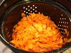 Carrot pieces in a strainer for blanching.