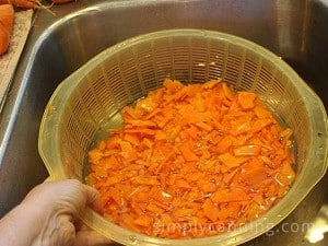 Cooling blanched carrot pieces and draining off the liquid in the sink.