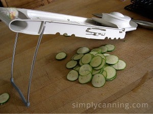 Slicing a zucchini into thin slices using the Mandolin slicer.