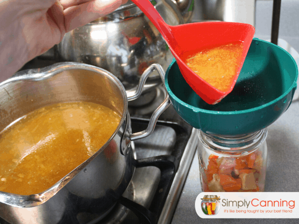 Pouring broth into a canning jar with solid ingredients already packed into it.