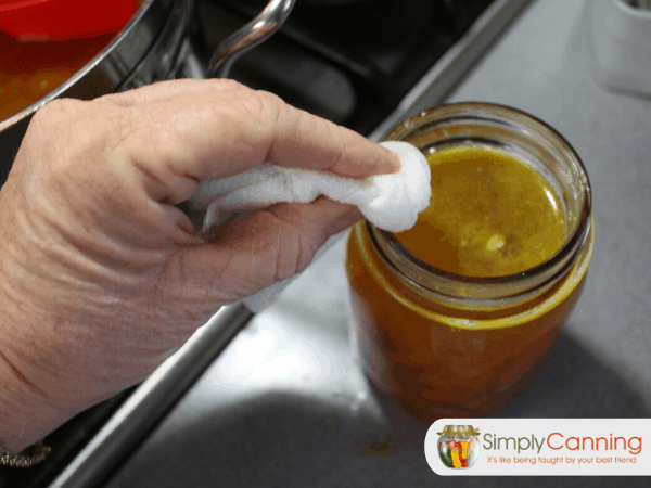 Wiping the rim of a jar filled with soup using a wet paper towel.