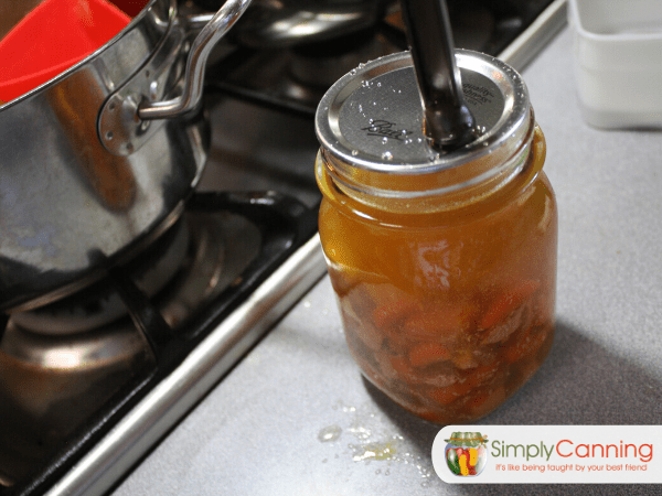 Using the magnetic lid lifter to place the flat lid on the jar filled with chicken soup.