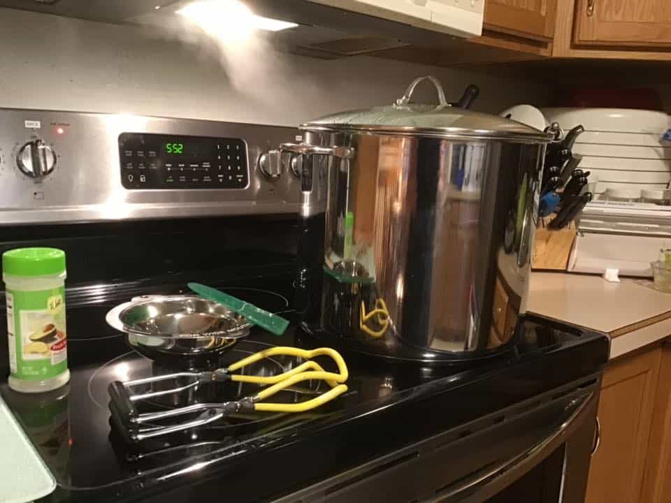 Canner and canning supplies on a black glass top stove.
