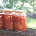 Three finished pint jars of zucchini in tomato sauce sitting on a deck railing.