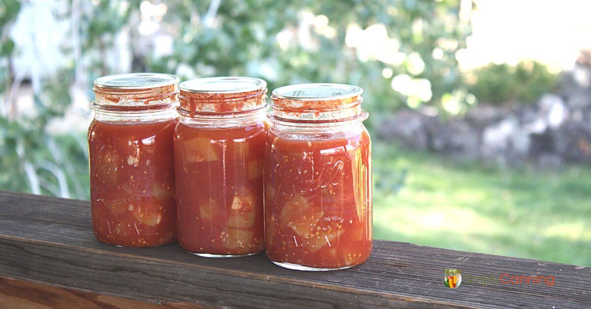 Three finished pint jars of zucchini in tomato sauce sitting on a deck railing.