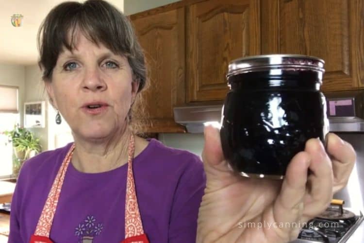 Sharon holding a small jar of cherry jam in her kitchen.