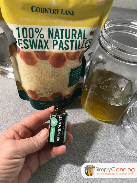 Holding a bottle of essential oils with beeswax pastiles and oil on the countertop behind.