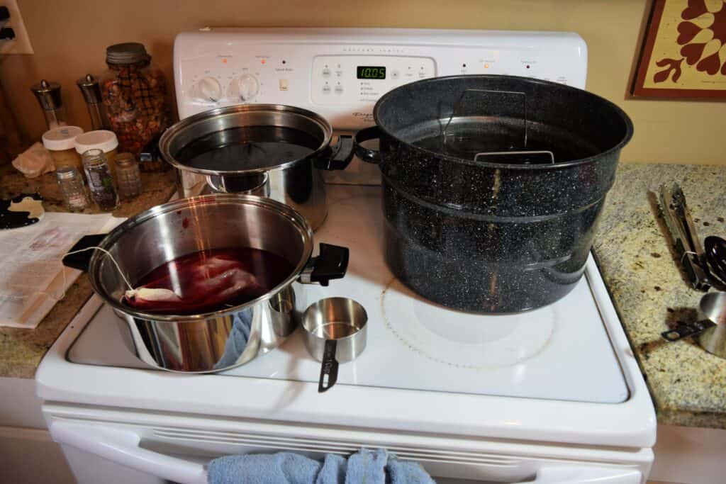 An open graniteware canner and other open pots sitting on a white glass top stove.