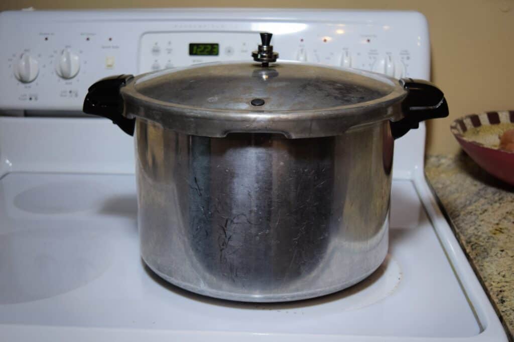 A small pressure cooker or canner sitting on a white glass top stove.