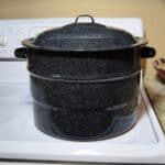 Speckled graniteware canner sitting on a white glass top stove.