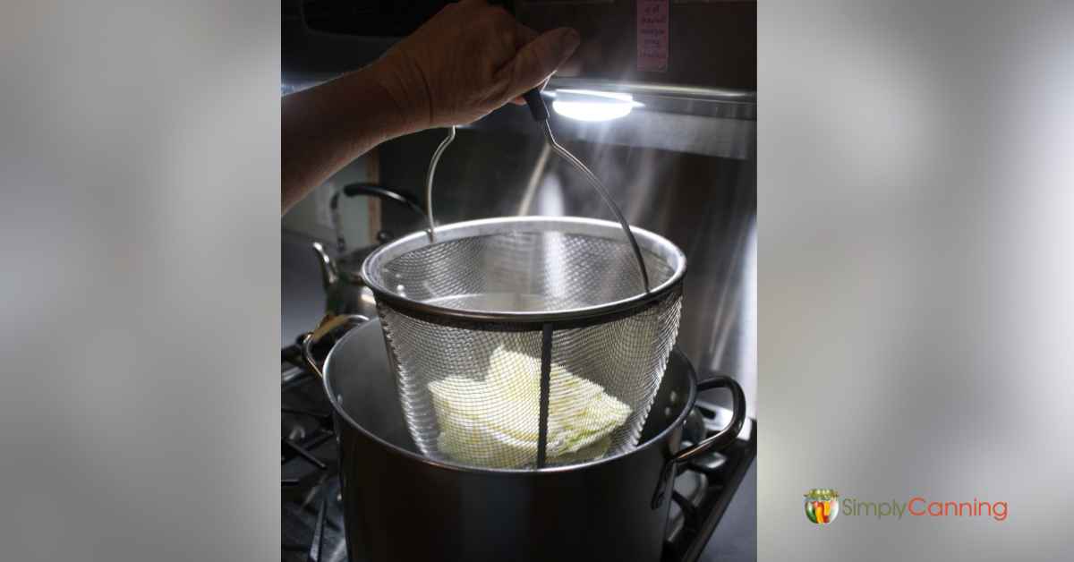 Lowering a blancher basket of cabbage wedges into a pot of boiling water.