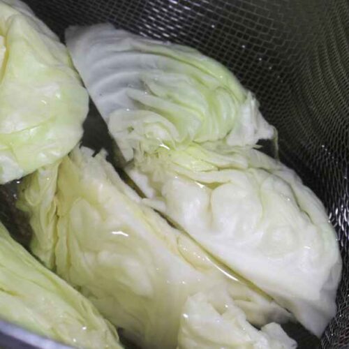 Wedges of cabbage in a blancher basket of water.