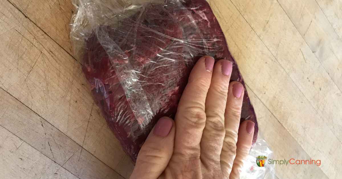 Pressing down a plastic wrapped package of ground meat.