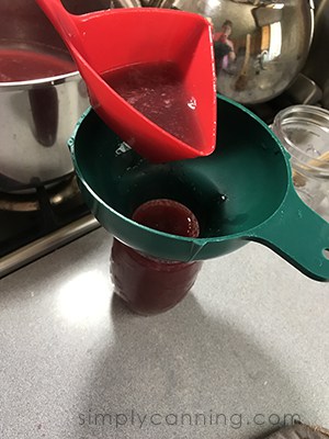 Ladling jam into a prepared jar through a canning funnel.