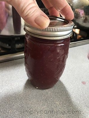 Tightening the screwband on a jar filled with grape jam.