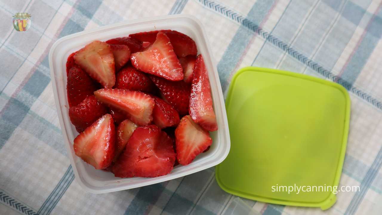 Top down view of square freezer container with strawberries, lime green lid sitting to the side.