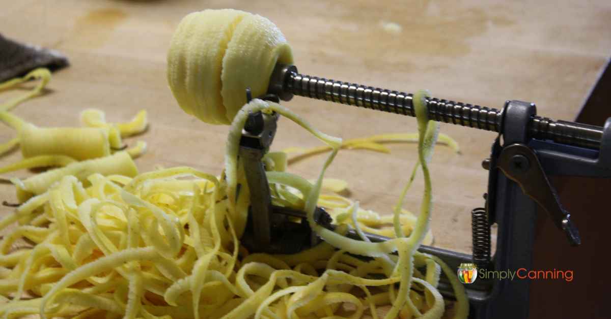  A peeled and sliced apple on the tool with a pile of peels and cores underneath it.