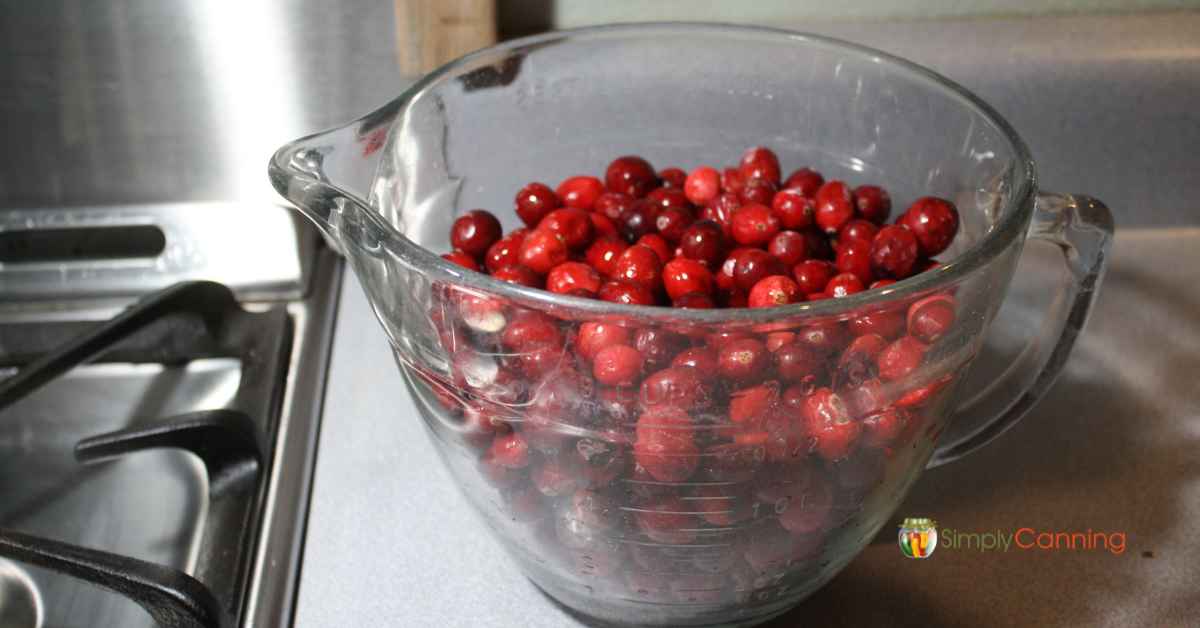  A large glass measuring cup full of fresh red cranberries.