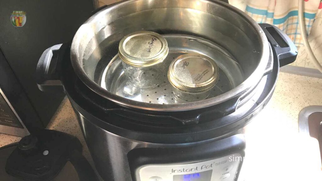 Top view of an open instant pot with 2 small canning jars and water. 