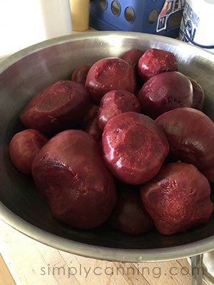Peeled whole beets sitting in a large stainless steel bowl.