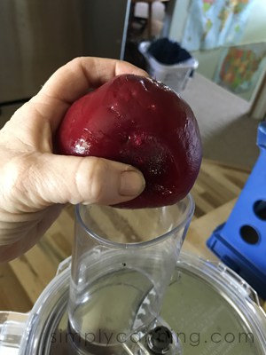 Dropping a whole peeled beet into the food processor chute.
