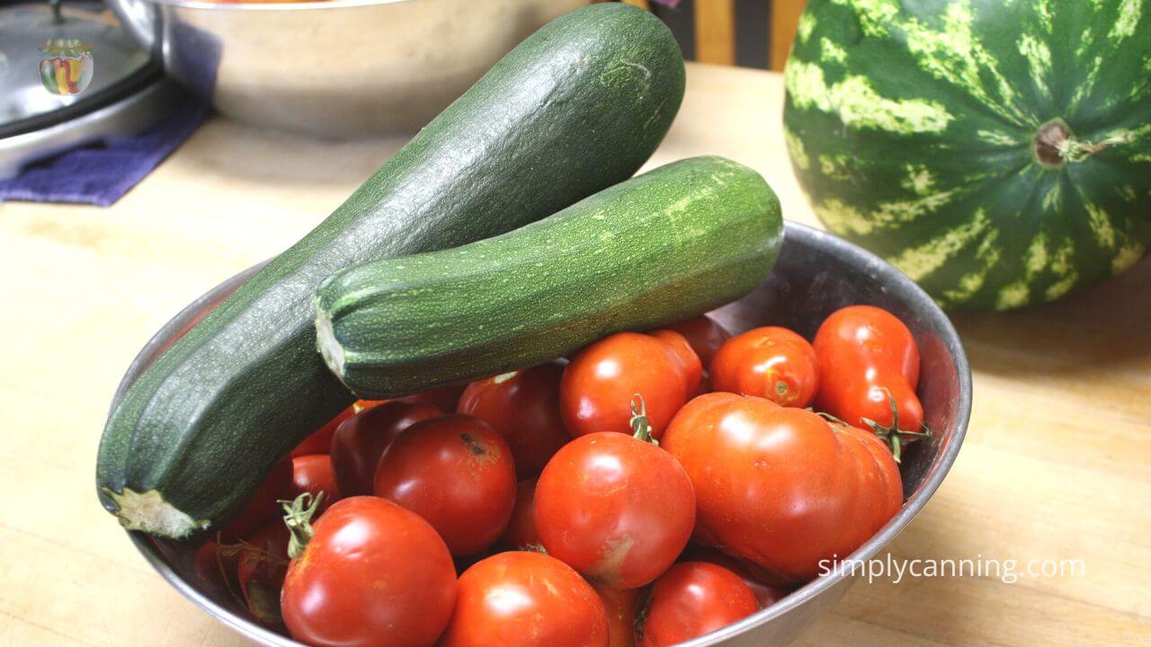 Stainless steel bowl with whole tomatoes and fresh zucchini