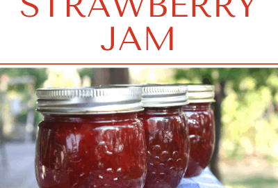 Jars of strawberry jam lined up on a blue and white checkered towel.