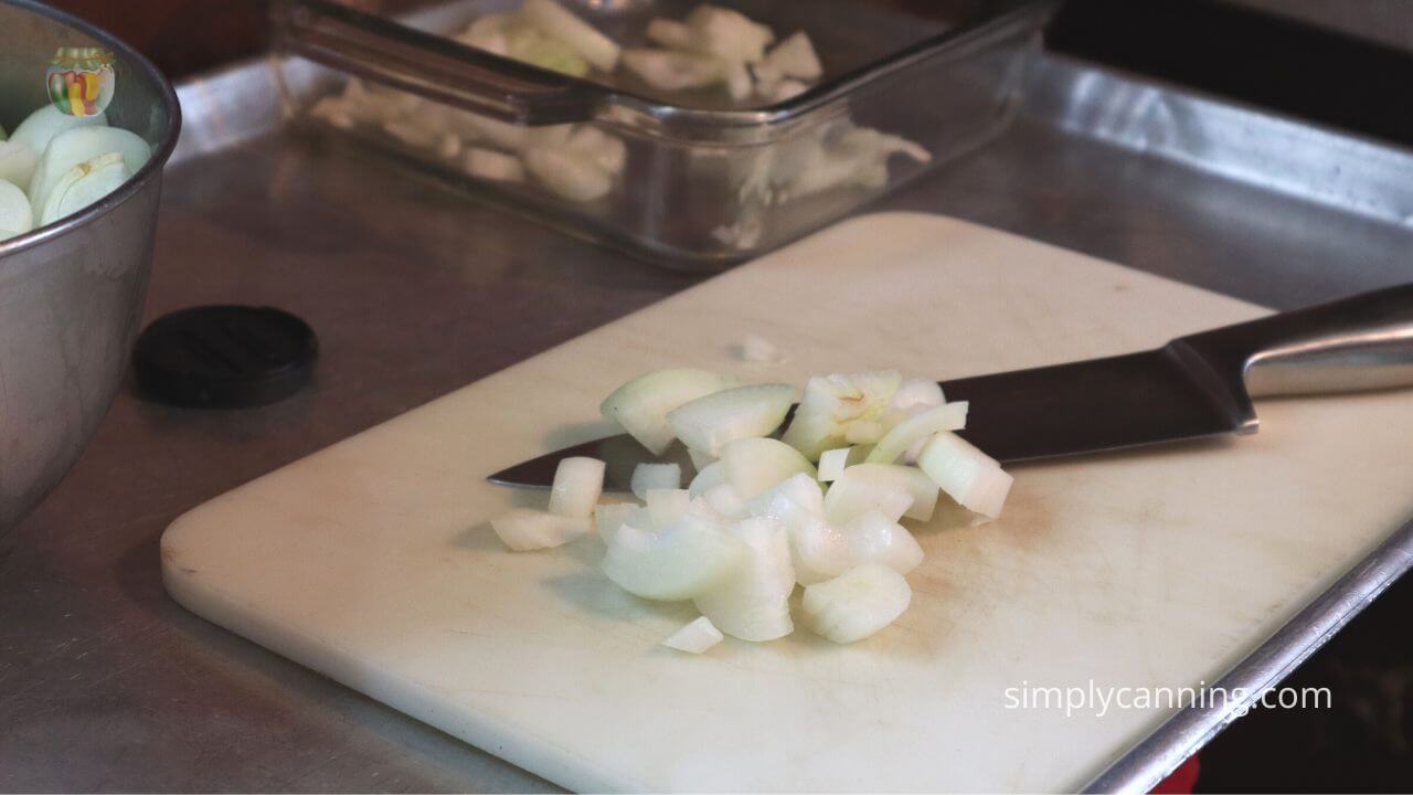 White cutting board with chopped white onions and a large knife. 