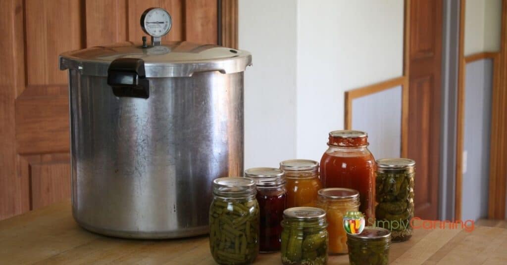 Pressure canner sitting on the countertop with various jars of food surrounding it.