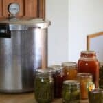 Pressure canner sitting on the countertop with various jars of food surrounding it.