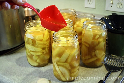 Topping off jars of apple pie filling using a ladle.