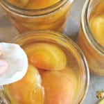 Wiping the rim of a jar filled with fresh apricot halves and syrup.