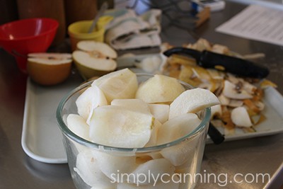 A bowl of peeled and sliced Asian pears with the scraps in the background.