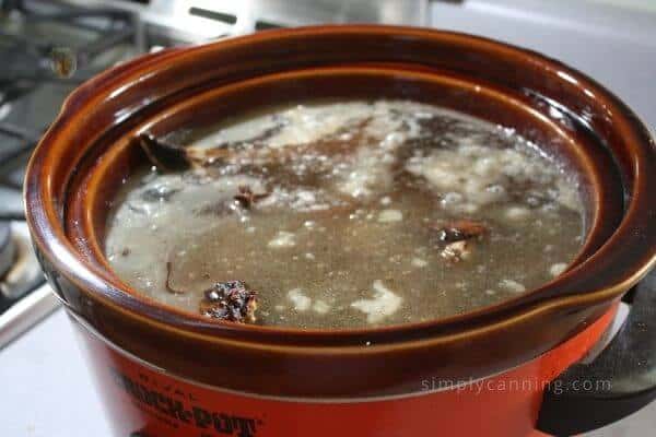 Gelatinous mixture of beef broth, meat, and bones cooking in a red slow cooker.