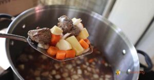 A serving spoon full of stew with carrots, beef, and potatoes.
