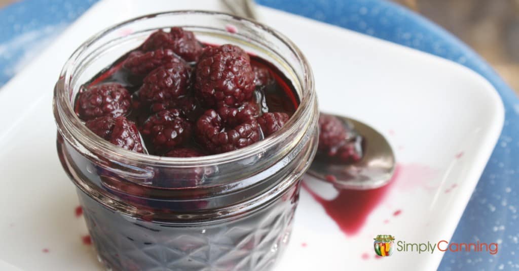 A small jar filled with juicy canned blackberries.