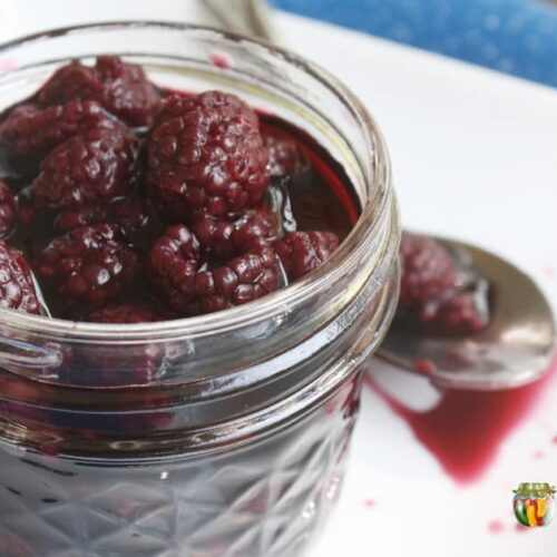 A small jar filled with juicy canned blackberries.