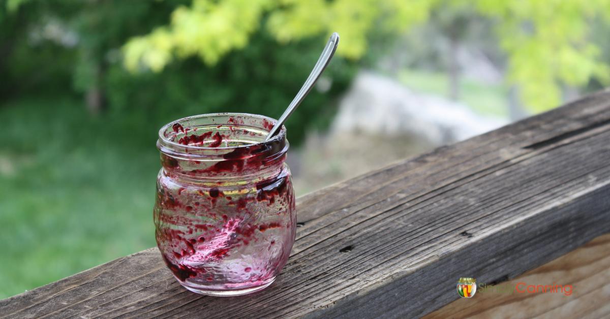 An empty jar of blueberry jam with a spoon sitting in it.