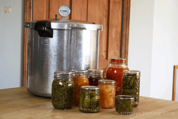 Pressure canner sitting on the countertop surrounded by jars of home canned food.