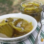 A bowl filled with bread and butter pickles with a jar sitting behind the bowl.