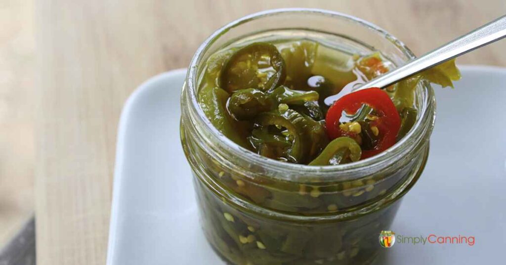 Small open jar of candied jalapenos with a fork in the jar.
